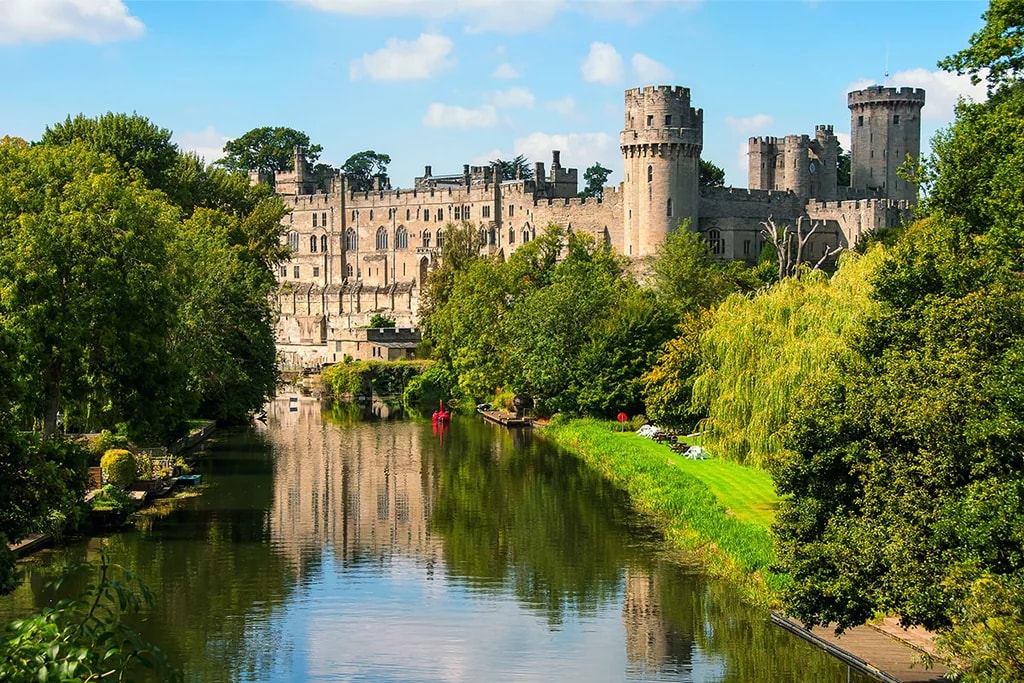 The image features the historic St. Mary's Castle in Stafford, England, with its stone structure, multiple towers, and multiple windows. The castle is surrounded by lush greenery and a tranquil river. The perspective is from the river, offering a panoramic view of the castle and its surroundings. The image code 'sa_1600' may refer to the specific viewpoint or angle.