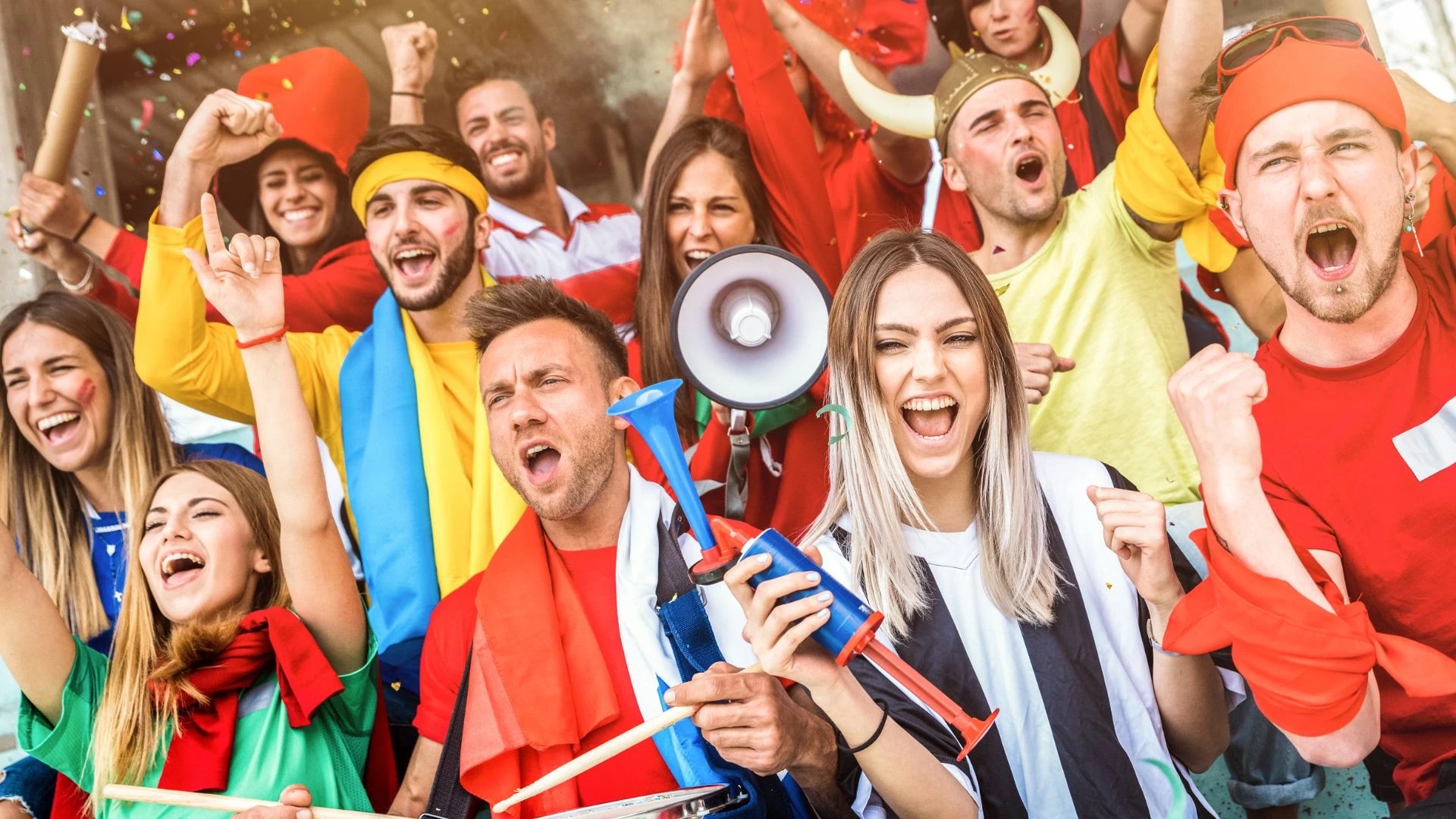 A lively soccer match scene features a diverse group of people in colorful attire, celebrating with flags and cheerleaders. The central figure, a man in a red and yellow shirt, holds a megaphone and waves, while others hold flags and cheerleaders. Confetti surrounds them, and the background is filled with confetti. The image captures the excitement and joy of a soccer match.