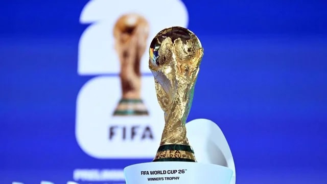 The image features the FIFA World Cup trophy, a gold-colored trophy with a black design, on a white base against a blue background. The trophy is the main focus, with a blurred background showing the FIFA logo and text. The text "FIFA World Cup 2018" is visible, indicating the event. The image captures the excitement and achievement of the FIFA World Cup.