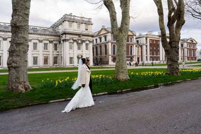 A couple in wedding attire walking in front of a grand building, capturing a joyful moment in a serene setting at Clarence Hall.