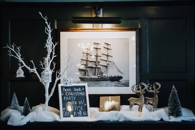 Christmas-themed mantel in Clarence Hall with a ship picture, silver deer statue, and lit candle, adding a festive touch to the wedding setting.
