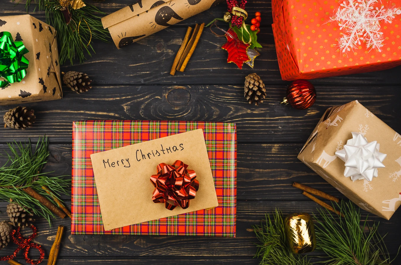 A festive scene features a red and plaid checkered gift bag with a "Happy Christmas" note, surrounded by red and green wrapped presents, pine cones, and a white bow. The dark wooden background contrasts with the colorful objects, creating a warm and festive atmosphere.