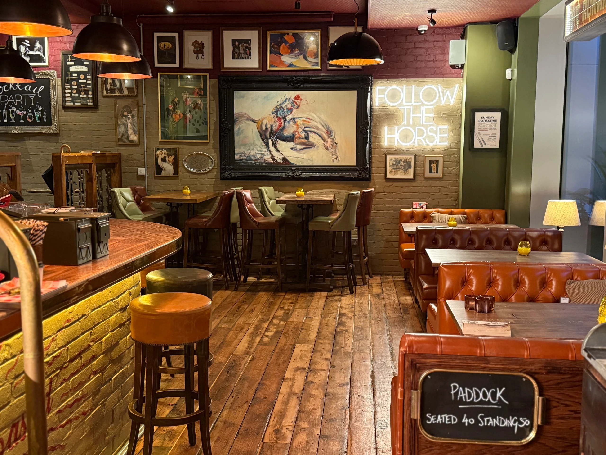 The image shows a cozy, rustic restaurant with a warm, inviting atmosphere. The wooden floor and brick walls create a rustic charm, while the bar and stools invite patrons to enjoy a drink. The walls are adorned with framed pictures and a chalkboard sign announcing "WORLD RACE". The arrangement of objects and lighting creates a harmonious balance, making the restaurant a welcoming and enjoyable place for visitors.
