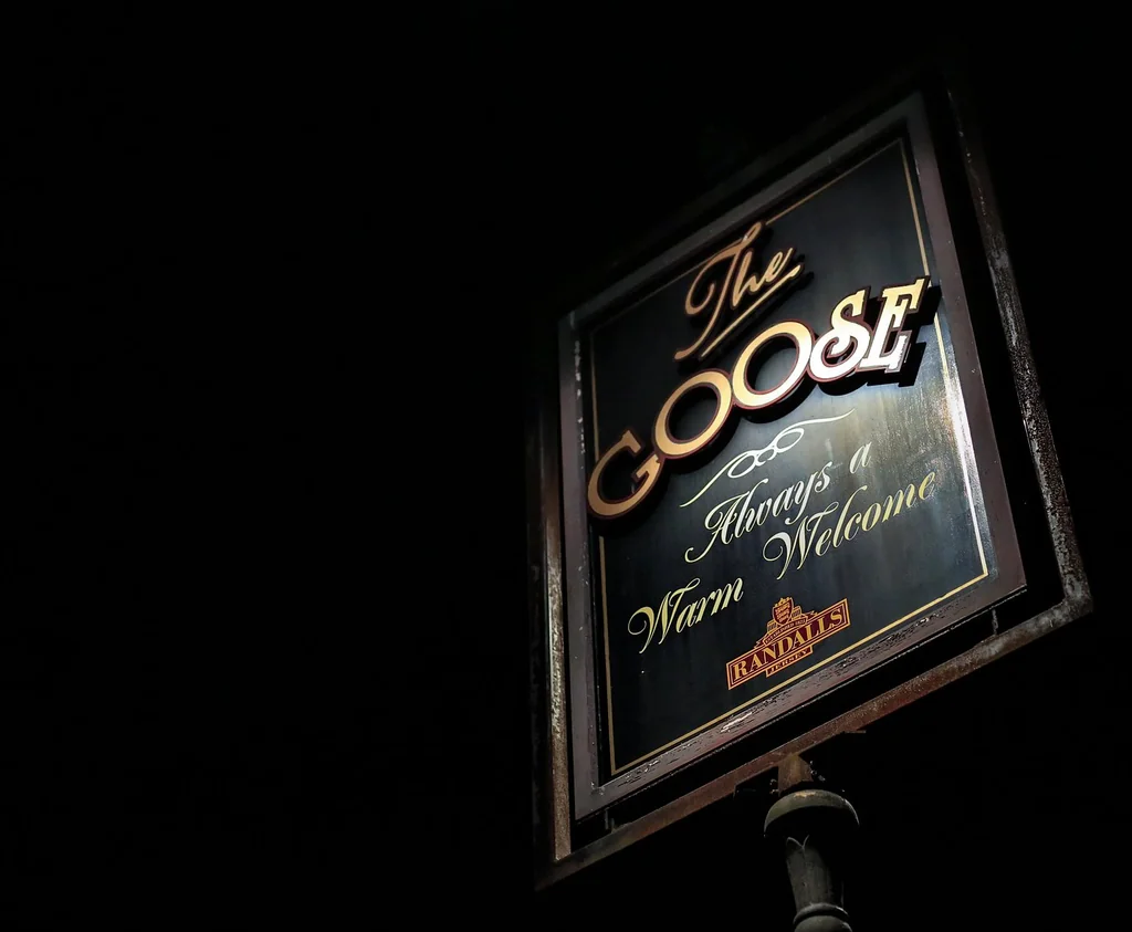 The image features a black sign with gold lettering for "The Book Store" and "The Book Shop" in gold, mounted on a black pole. The sign is illuminated by a light source, casting a warm glow. The background is dark, emphasizing the sign's prominence. The text is clear and legible, with no other objects or actions. The sign is the main subject, with the background serving as a backdrop.