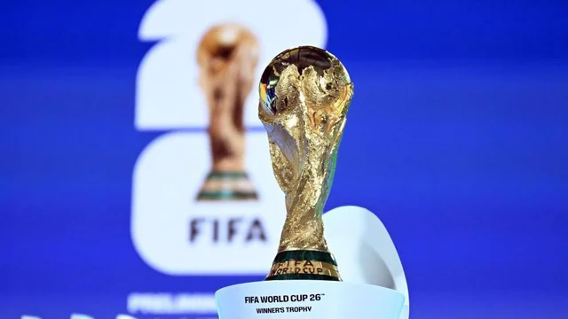 The image features the FIFA World Cup trophy, a gold-colored trophy with a black design, on a white base against a blue background. The trophy is positioned in the foreground, with a blurred background showing the FIFA logo and text. The text "FIFA World Cup 2018" is visible, indicating the year of the event. The image captures the excitement and achievement of the FIFA World Cup.
