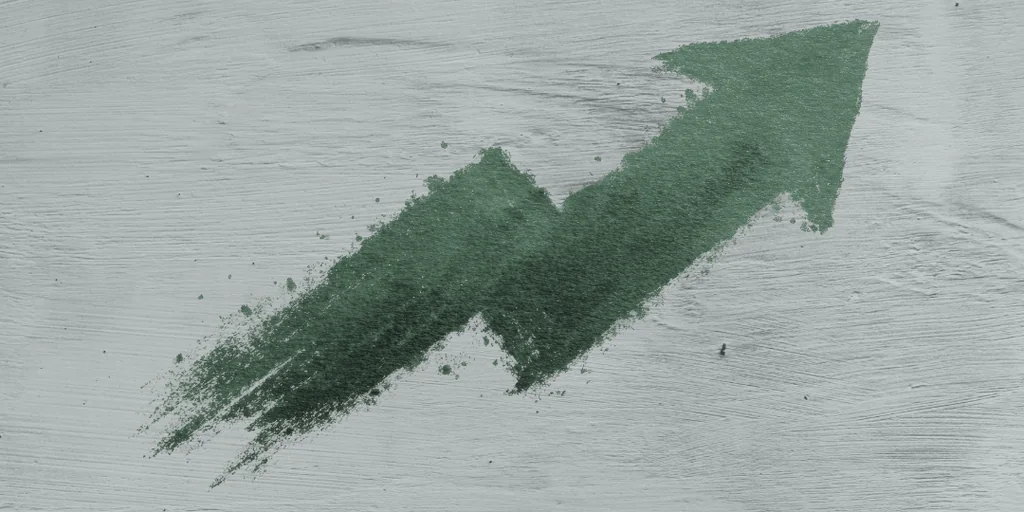 A green, jagged-pointing arrow on a gray wooden surface, pointing upwards, creates a sense of direction and progress.